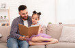 © Prostock-studio - Caring daddy reading book to his cute daughter