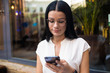 © ZoFot - Charming dark hair woman in trendy glasses online shopping store via mobile phone during recreation time. Hipster girl in glasses using apps on cellphone