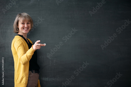 Fotomural Young teacher with piece of chalk is standing near blackboard in a classroom