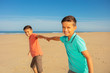 Two boys play on the beach running pulling hands