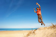 Boy jumps from sand dune on a beach rising hands