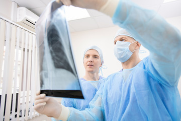 Two professional pulmonologists in protective uniform looking at x-ray of lungs