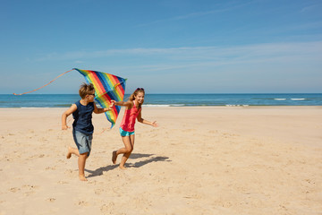 Wall Mural - Two kids boy and girl run with color kite on beach