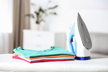 Sticker - Modern electric iron and clean folded clothes on board in room. Space for text