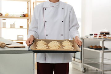 Wall Mural - Female pastry chef holding baking sheet with uncooked croissants in kitchen, closeup