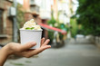 Woman holding cup with tasty frozen yogurt outdoors, closeup. Space for text