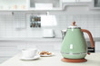 Modern electric kettle, cup and cookies on wooden table in kitchen