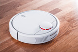 Fototapeta Na ścianę - white robotic vacuum cleaner in rays of morning sun. robot controlled by voice commands for direct cleaning. modern smart appliance for cleaning house