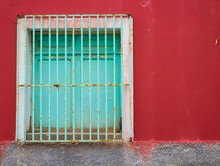 Green Barred Closed Window In A Red Wall.