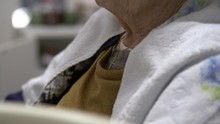 Elderly Female Sitting, Wearing Small Christianity Crucifix Necklace. Shallow Focus.