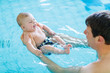 © Irina Schmidt - Happy middle-aged father swimming with cute adorable baby in swimming pool.