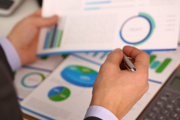 Male hand in suit hold siver pen in office with clipboard on table closeup. Comprehensive audit of enterprise business at all stages development.