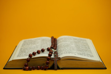 Open Holy Bible with old beads on a yellow background table. Religion concept.