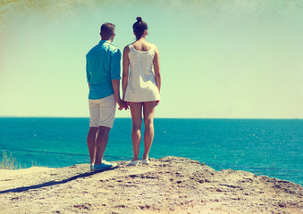 A young couple stands on the edge of a cliff and looks at the sea