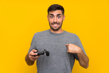 Wall Mural - Young handsome man playing with a video game controller over isolated yellow background with surprise facial expression