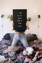 Hipster Woman Holding A Blackboard With A Funny Text. Time To Renew A Woman Wardrobe. Messy Woman Trying To Decide What To Wear. Fashion And Blogger Lifestyle. Bed Full Of Seasonal Clothes.