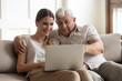 © fizkes - Grandfather and adult granddaughter sitting on couch using laptop