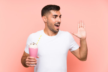 Young man with strawberry milkshake over isolated pink background shouting with mouth wide open