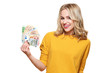 © andreaobzerova - Young pretty woman in yellow sweater holding bunch of Euro banknotes, looking at camera and smiling, isolated on white background.