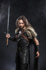 Wall Mural - Portrait of a courageous ancient warrior in armor with sword and shield. Concept historical photo of bravery knight with long sword