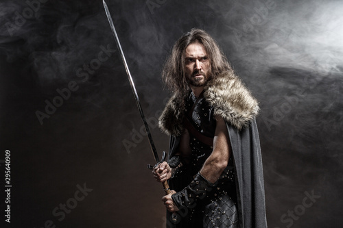 man-dressed-in-medieval-armor-and-raincoat-with-longs-word-fighting-against-enemy-courage-fantasy-warrior-knight-with-long-hair-concept-historical-photo