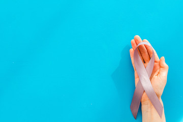 Disease control concept. White ribbon in hands on blue background top view copy space