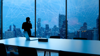 Businessman standing using smart phone and Business Wireless network in office desk and windows and Bangkok city view.