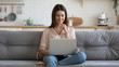© fizkes - Smiling young woman using laptop, sitting on couch at home