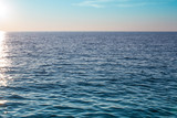 Fototapeta  - Horizon on the sea. Sun reflects in the water in the small waves. A pair of white clouds are hanging over the water.