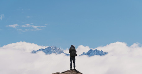 Wall Mural - a man with backpack standing on mountain top, with snow mountains over clouds. success, achievement 