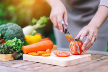 Closeup Image Of A Woman Cutting And Chopping Tomato By Knife On Wooden Board