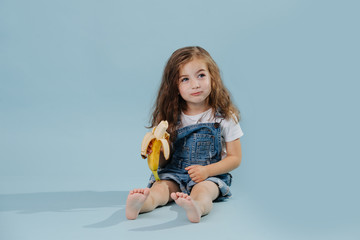 Toddler girl eating banana, studio portrait on blue background