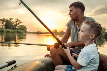 Happy Father and Son together fishing from a boat at sunset time