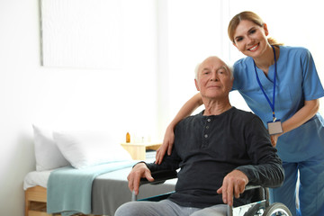 Canvas Print - Nurse assisting elderly man in wheelchair indoors. Space for text