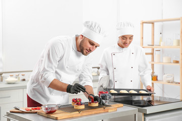 Pastry chefs preparing desserts at table in kitchen