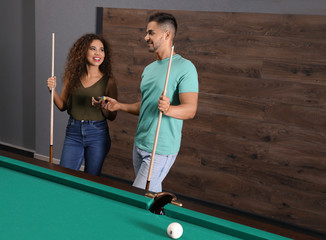 Wall Mural - Young man and woman playing billiard indoors