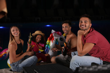 Wall Mural - Happy young friends with refreshing cocktails relaxing near outdoor pool at night