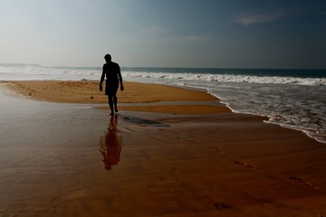 Sticker - Man's silhouette walking on a beach near a body of water with waves