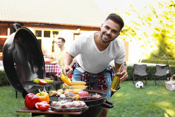 Canvas Print - Young man with beer cooking on barbecue grill outdoors