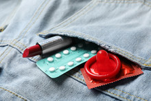 Red lipstick with condoms and birth control pills in pocket of jeans, closeup. Safe sex concept