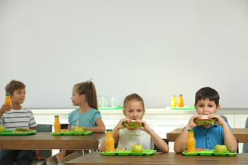 Happy children eating healthy food for lunch in school canteen