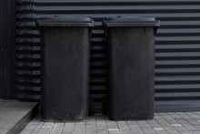 two scratched black dustbins against black metal corrugated wall