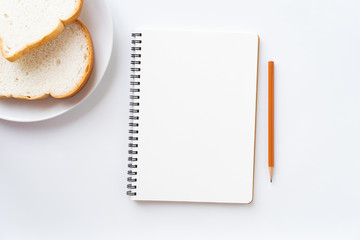 Wall Mural - top view of blank notebook on the table. bread in a plate and pencil on a white ground