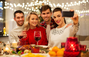 Wall Mural - holidays and celebration concept - happy friends taking selfie by smartphone at home christmas dinner