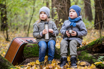 Children playing in autumn forest full of yellow leaves with vintage suitcase.