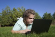 © ShapikMedia - Teenage girl  working on a laptop on green grass. Distance learning. Girl with a laptop on a background of pines. Girl with a computer on the street.