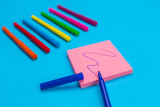 Fototapeta  - Photo of colorful bright felt-tip pens lying in the left corner on a blue background next to which is a set of pink stickers with a blue felt-tip pen. Close-up.