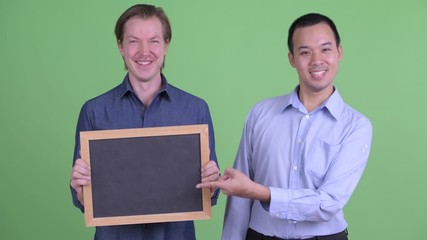 Canvas Print - Two happy multi ethnic businessmen holding blackboard and giving thumbs up