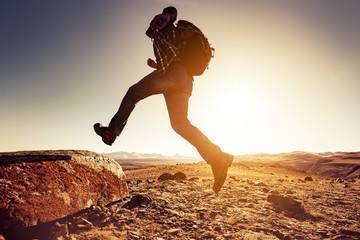 Wall Mural - man with backpack jumps to big rock