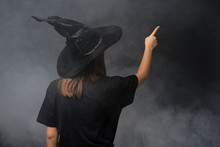 Girl With Witch Costume For Halloween Parties Over Isolated Dark Background Pointing Back With The Index Finger